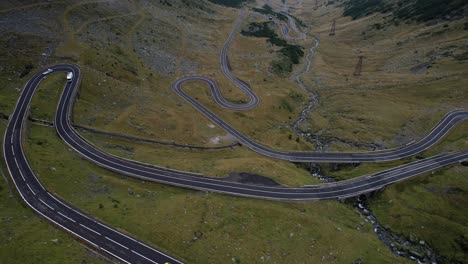a graceful left-to-right sweep reveals the winding curves of transfagarasan road, weaving through lush green mountains in romania under a moody summer sky.