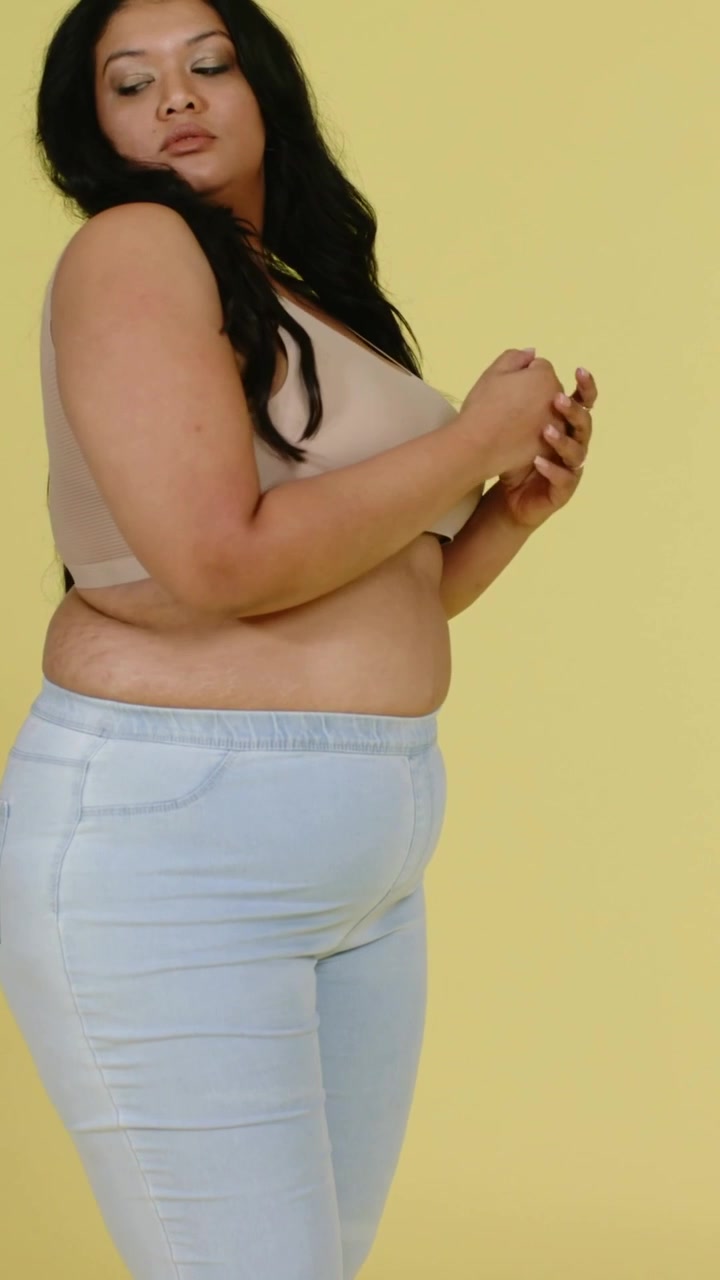 Video verticale: Modella che ruota posando per un servizio fotografico in studio, con sfondo giallo, indossando un top beige e jeans.