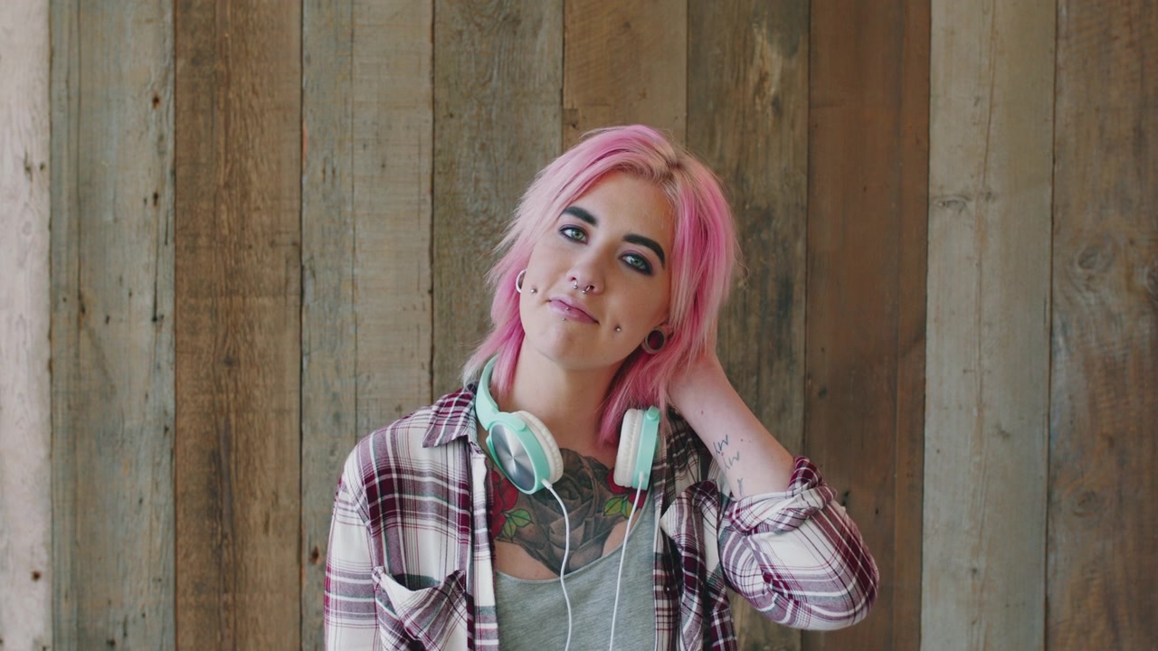 Giovane donna con capelli rosa e piercing in posa contro una parete di legno