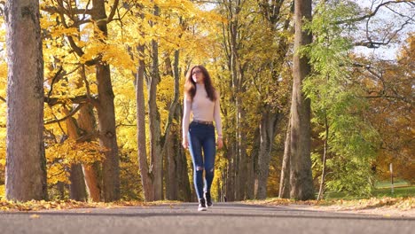 mujer joven caminando por un camino en un parque público bajo árboles en colores amarillos de otoño