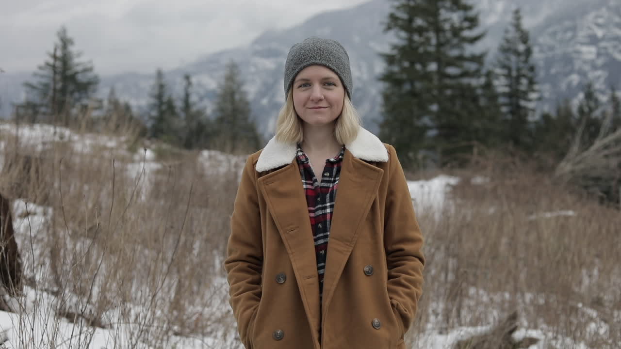 A girl stands in a meadow with snowy mountains around her.