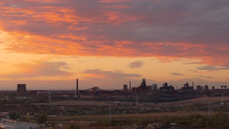 aerial close up shot showing distant industrial area, vibrant orange-clouded sunset, offering a striking industrial landscape, 4k50fps