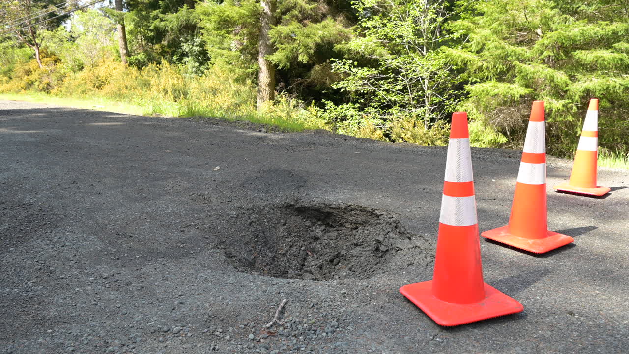 Large sinkhole from a broken culvert on a rural street. Traffic cones blocking traffic.