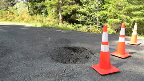 large sinkhole from a broken culvert on a rural street. traffic cones blocking traffic.
