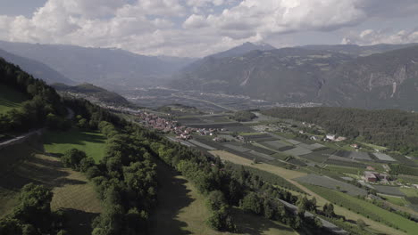 Drone-shot-from-Tesimo-Italy-looking-over-the-valley-of-Bozen-in-between-the-hills-and-mountains-on-a-sunny-but-cloudy-day-with-clouds-LOG