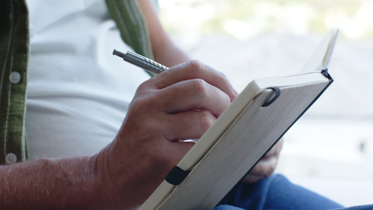 Right hand is lowering silver pen, making short notes and adjusting grip in notebook near window