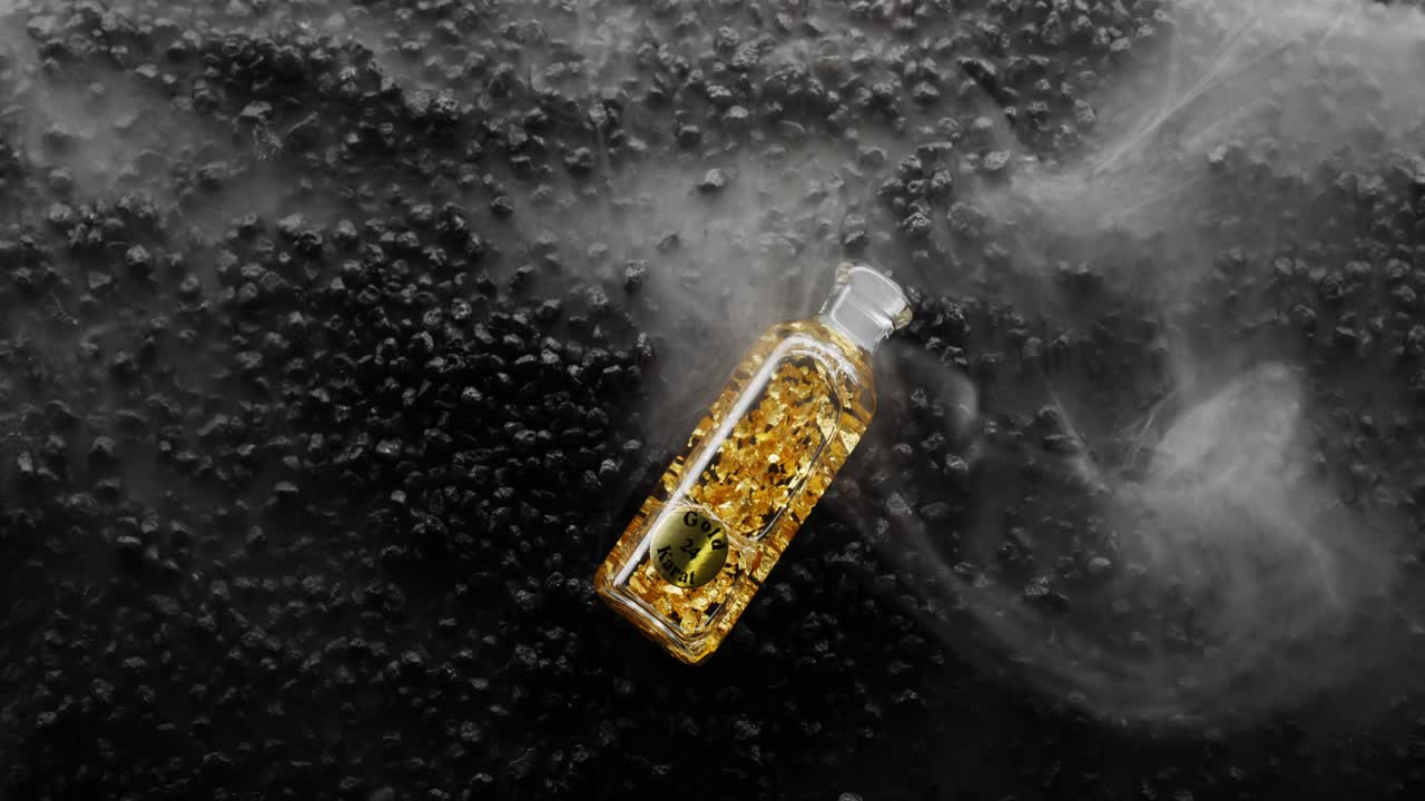 Bottiglia d'oro 24k che cade in un mare di fumo su un letto di rocce nere