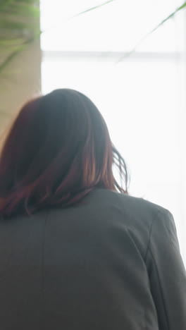 Profile view of businesswoman in gray blazer standing in brightly lit office corridor, looking forward with focused expression, suggesting determination, leadership, and clear sense of direction in workplace