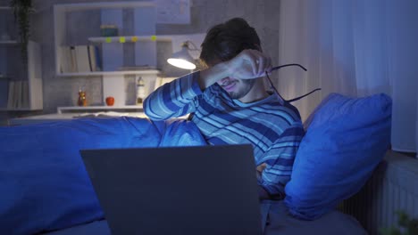 Young-man-working-with-laptop-in-bed.-He-is-tired-and-sleepy.