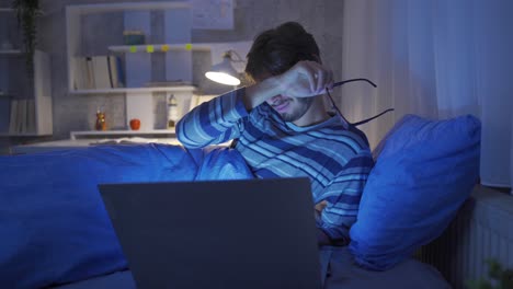 joven trabajando con una computadora portátil en la cama. está cansado y con sueño.