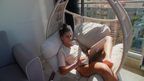 woman working from home on a balcony in a hanging chair