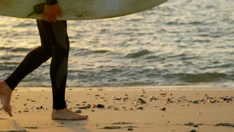 side view of mid-adult caucasian male surfer walking with surfboard at the beach 4k