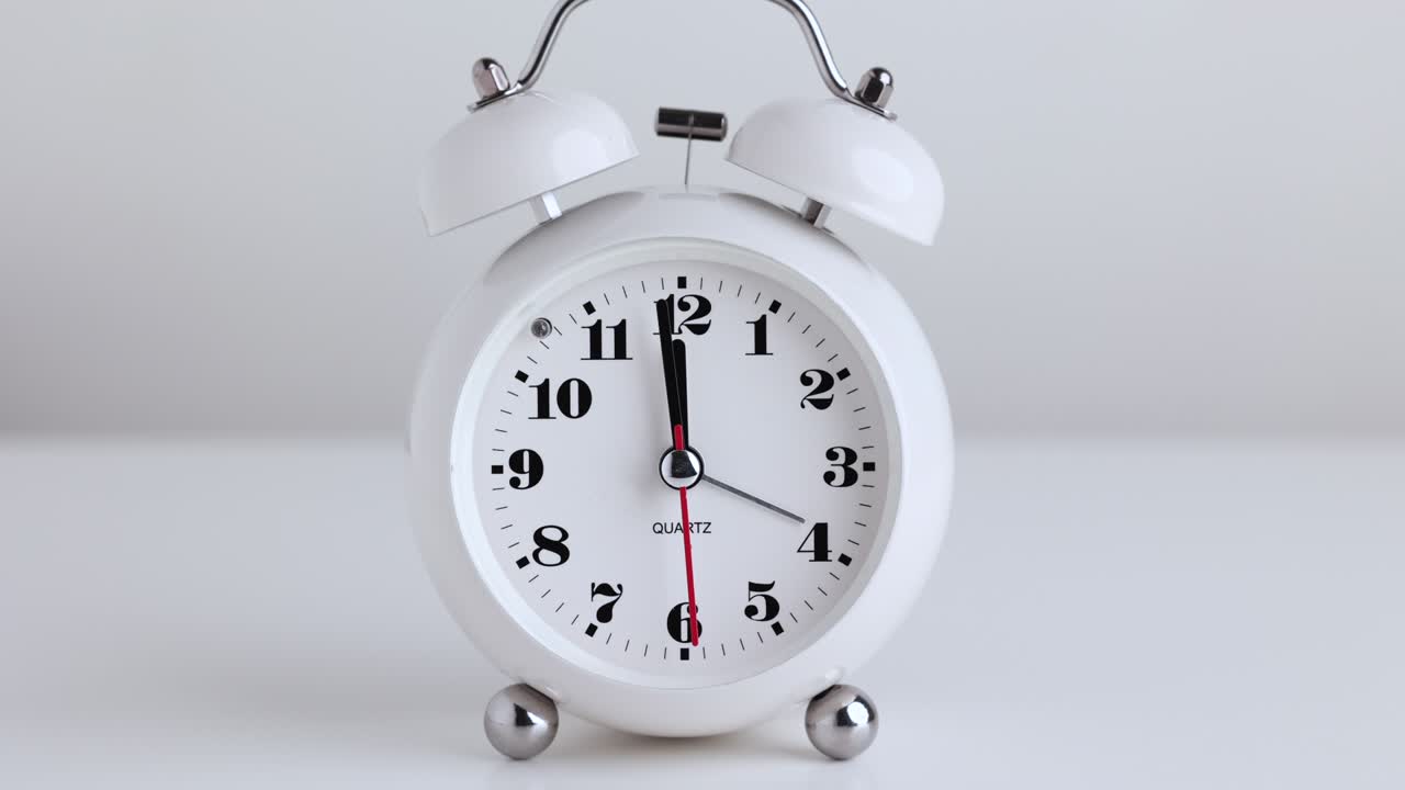 película de lapso de tiempo. pequeño despertador blanco, números negros, fijar la hora para las doce, colocado en una mesa blanca.