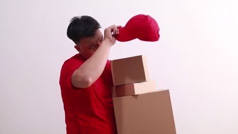 sad young asian courier man holding cardboards and feeling hot weather in the summer day in studio