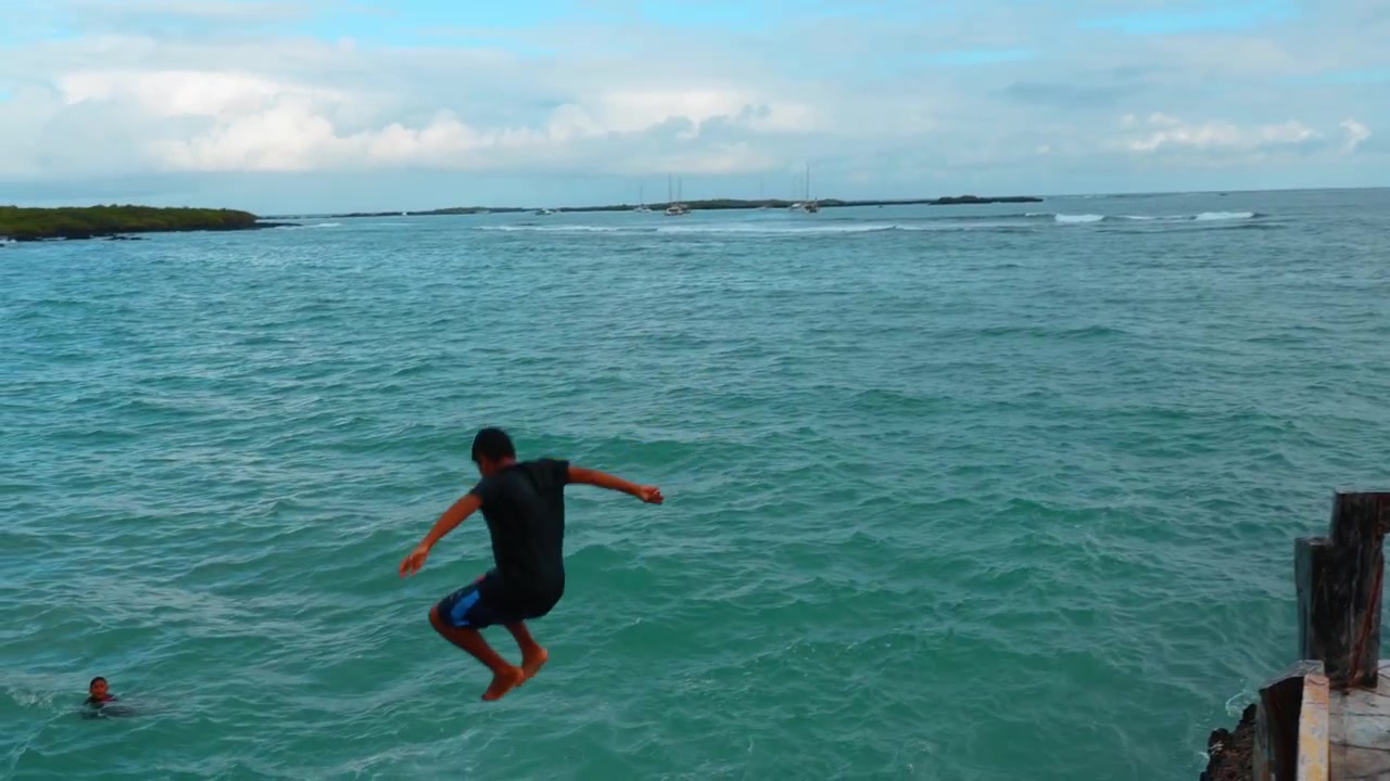 Santo Tomas, Ecuador, 1 maggio 2026: Persona che nuota in acqua oceanica turchese vicino al porto con barche. Ampia vista dell'Oceano Pacifico turchese con una persona che nuota e spruzzi d'acqua bianca sull'Isola Isabela