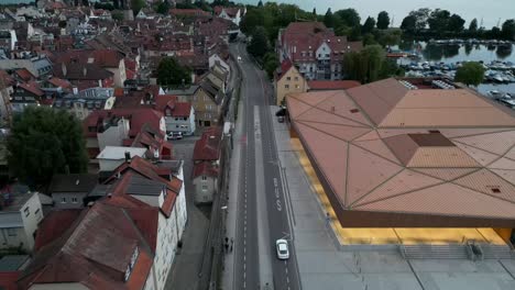 drone footage spans a road with commercial and residential buildings on the left and a harbor filled with boats on the right, offering stunning views