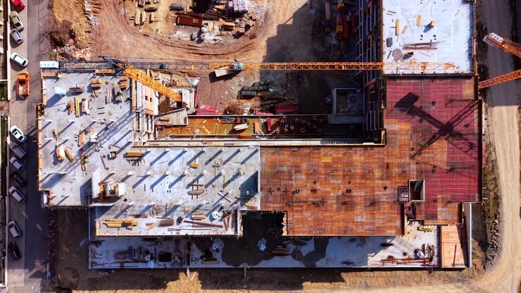 Rebar flooring at building site. Top down drone shot of construction materials, crane arm and a parked van on bare earth.
