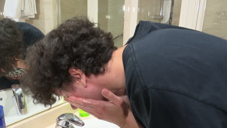young man washing face in hotel bathroom