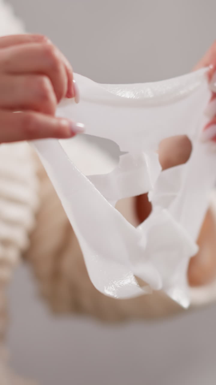 mujer sostiene una máscara facial con consistencia líquida en las manos. mujer con manicura en bata de baño a punto de ponerse una máscara de tela facial de pie en el baño