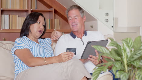 senior diverse couple shopping online with tablet and credit card, smiling at home