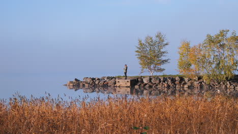 man enjoys autumn weather on lake coastline in scandinavia, distance view