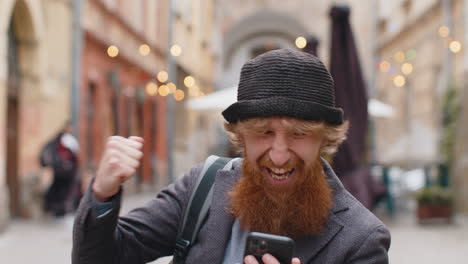 Young man use mobile smartphone celebrating win good message news outdoors in urban city street