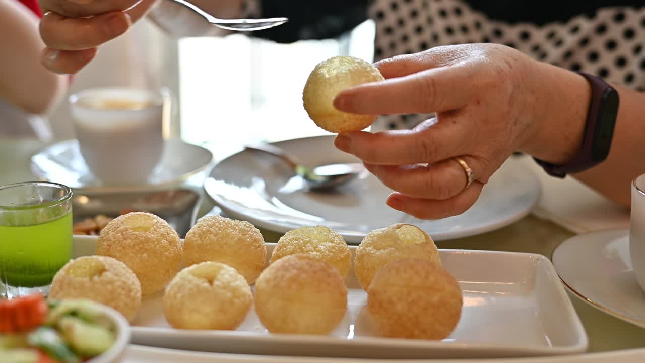 un primer plano de una mujer llenando salsa de chile en el hueco de panipuri, una popular comida callejera india.