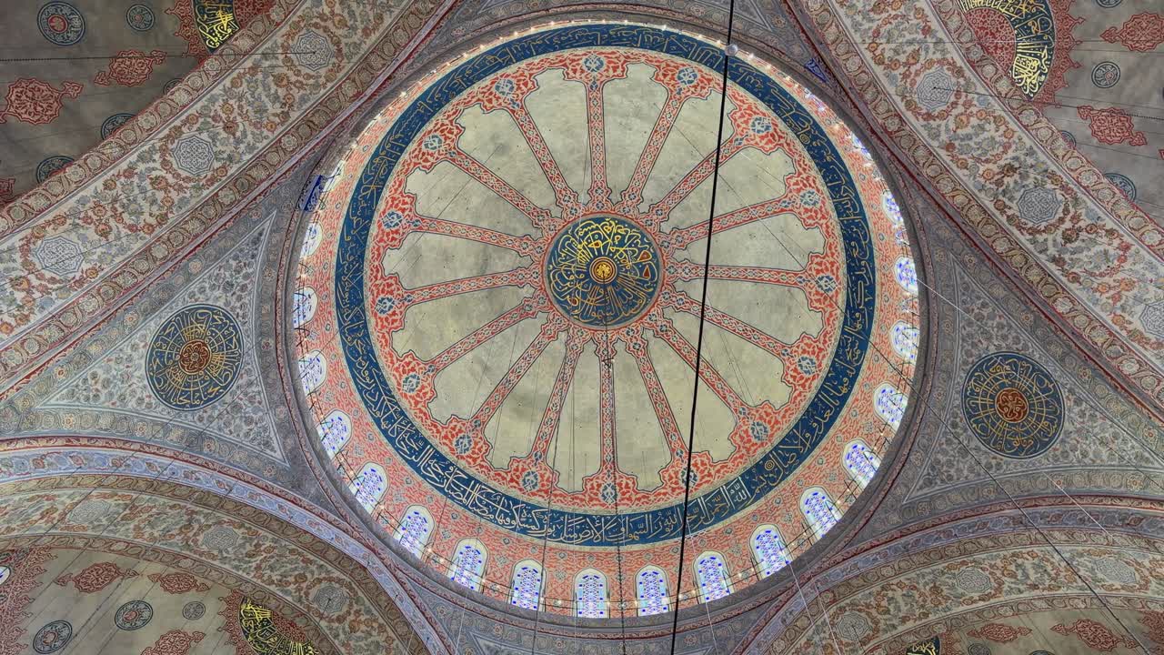 Ripresa cinematografica in 4K che guarda in alto verso il magnifico soffitto della Moschea Blu a Istanbul. Mette in mostra gli intricati motivi ottomani, le splendide vetrate e i massicci lampadari.