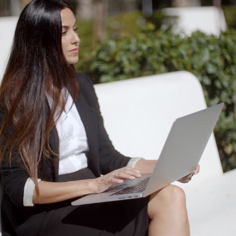 Young-woman-using-a-laptop-on-a-white-park-bench