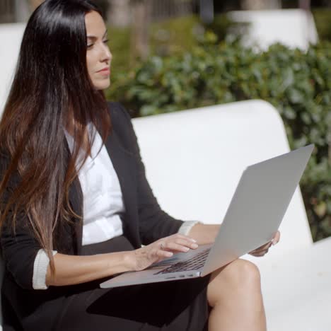 young woman using a laptop on a white park bench