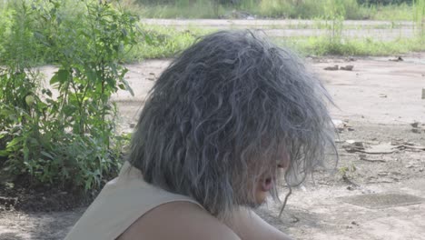 the video features an elderly person sitting outdoors, talking to themselves, with a background of trees and wasteland, creating a desolate atmosphere