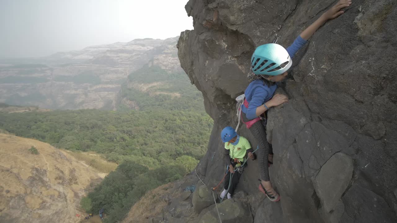 Wide shot young Indian girl attempting to rock climb a beautiful pinnacle on sunny day
