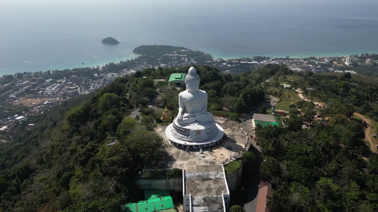 Descending half-orbit drone shot approaching the white marble Big Buddha. Features breathtaking views of the Andaman Sea and Phuket's tropical coast in the background. 4K cinematic travel footage