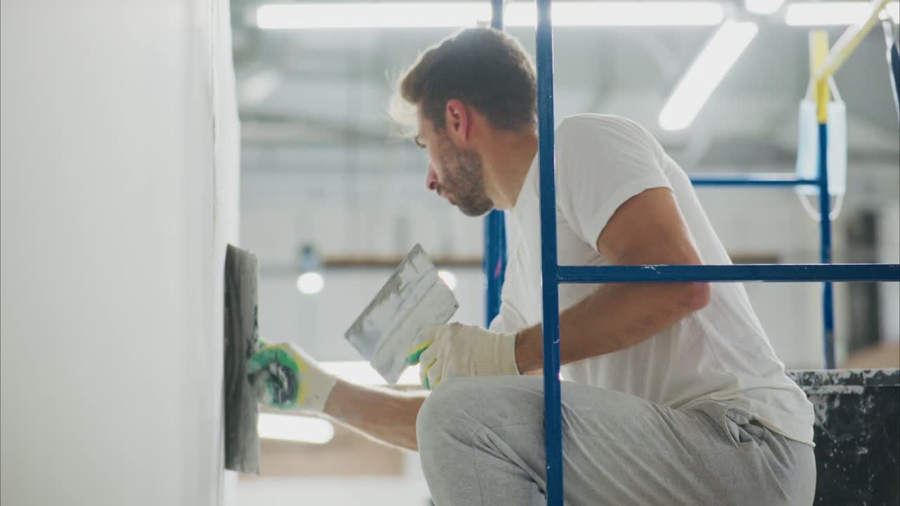 Professional Painter Working on Wall Restoration from Scaffolding: Skilled Craftsman Applying Finishing Touches to the Surface with Precision Tools in a Renovation Project