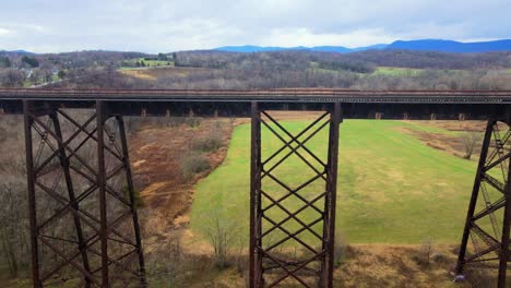 aerial drone video footage of a train bridge viaduct running over a valley in the appalachain mountains during early spring on a cloud day, surrounded by mountains and farmland