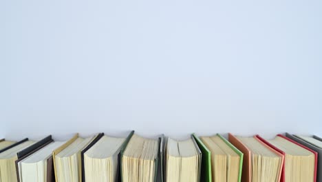 una pila de libros de tapa dura de diferentes colores se mueve en una estantería con espacio vacío para el texto.