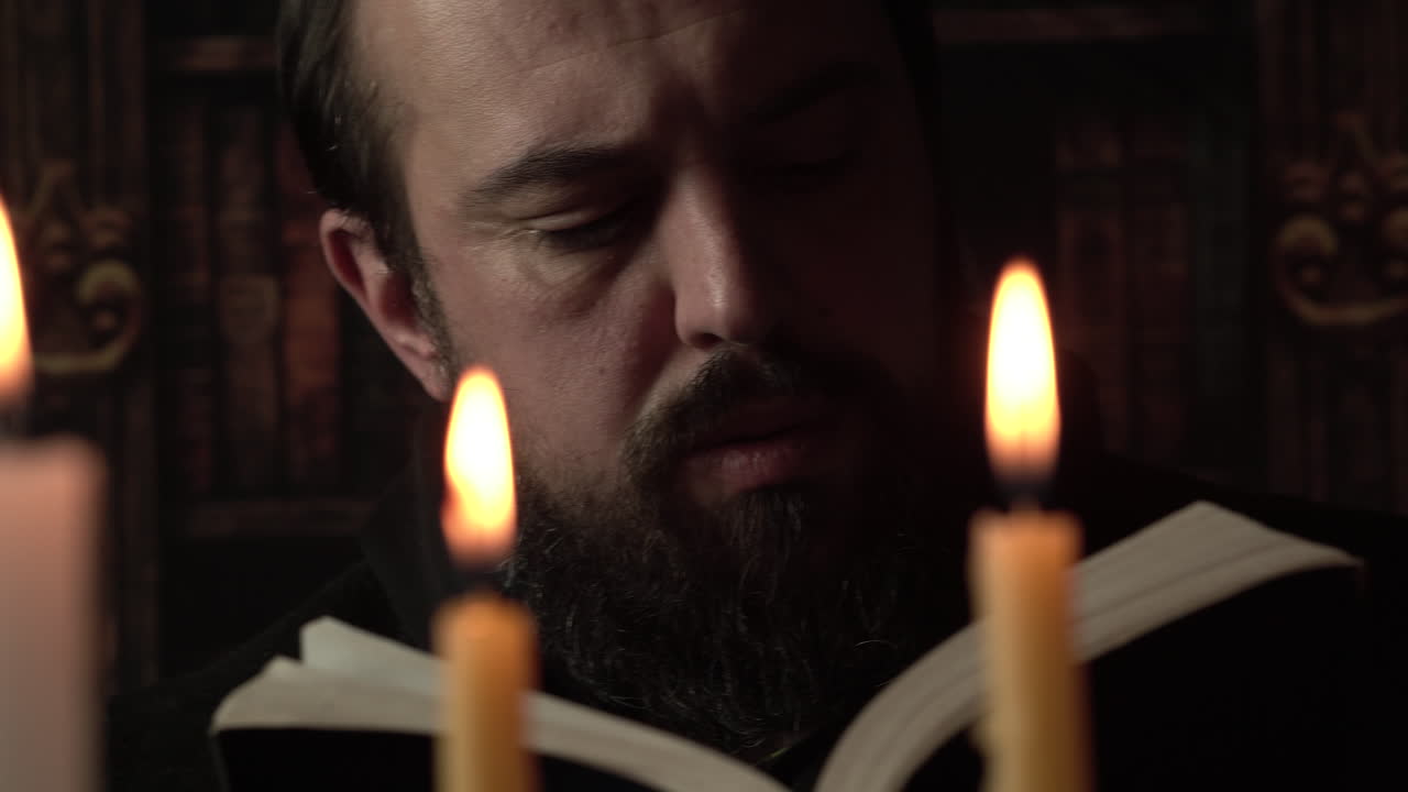 Uomo medievale che legge un libro a lume di candela, primo piano.