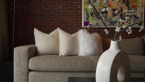 panning-tight-shot-of-white-pillows-on-a-grey-couch-in-a-living-room-with-brick-walls