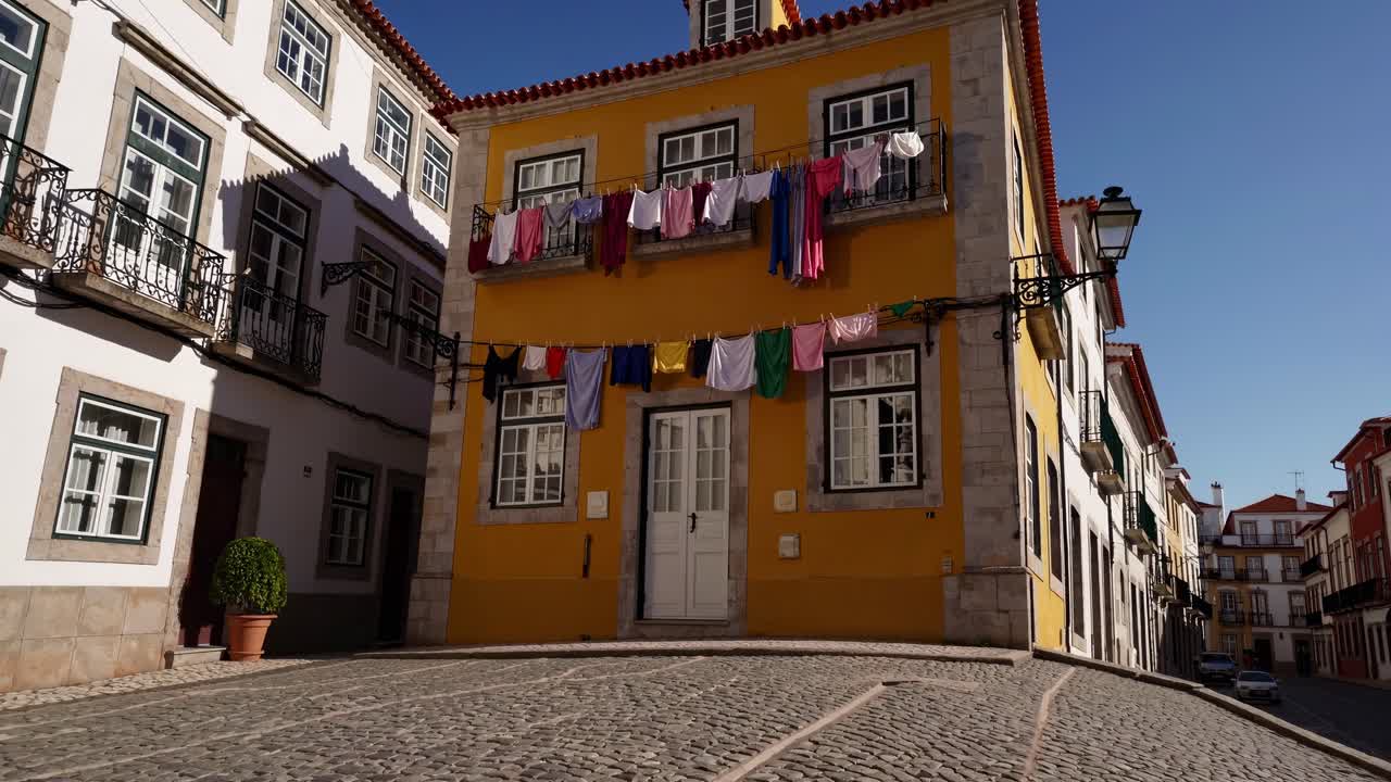 Laundry hanging from the windows and balconies of colorful houses in a historic Portuguese town, creating a vibrant and picturesque scene under the clear blue sky