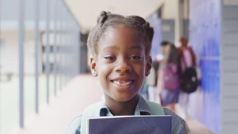 Portrait-of-happy-african-american-schoolgirl-walking-in-school-corridor