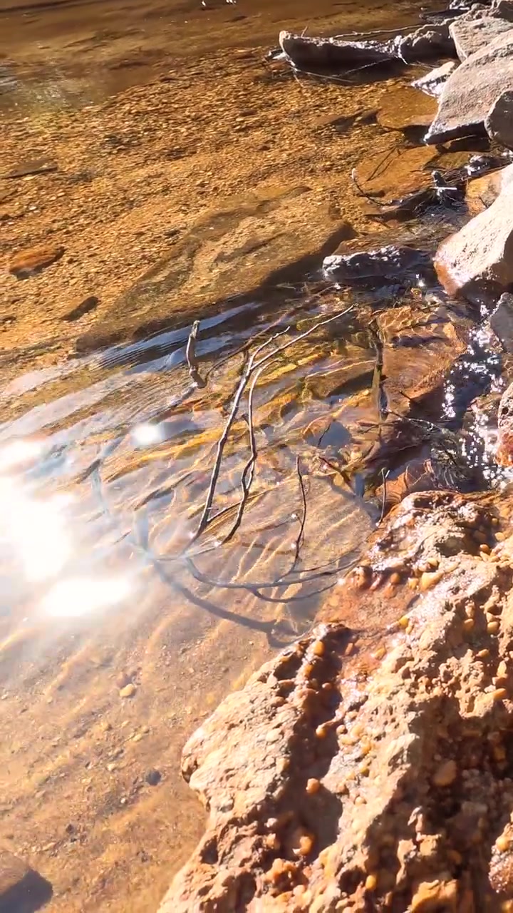 Clear water flows over orange rocks with bright sunlight reflections in Wentworth Falls, Australia.