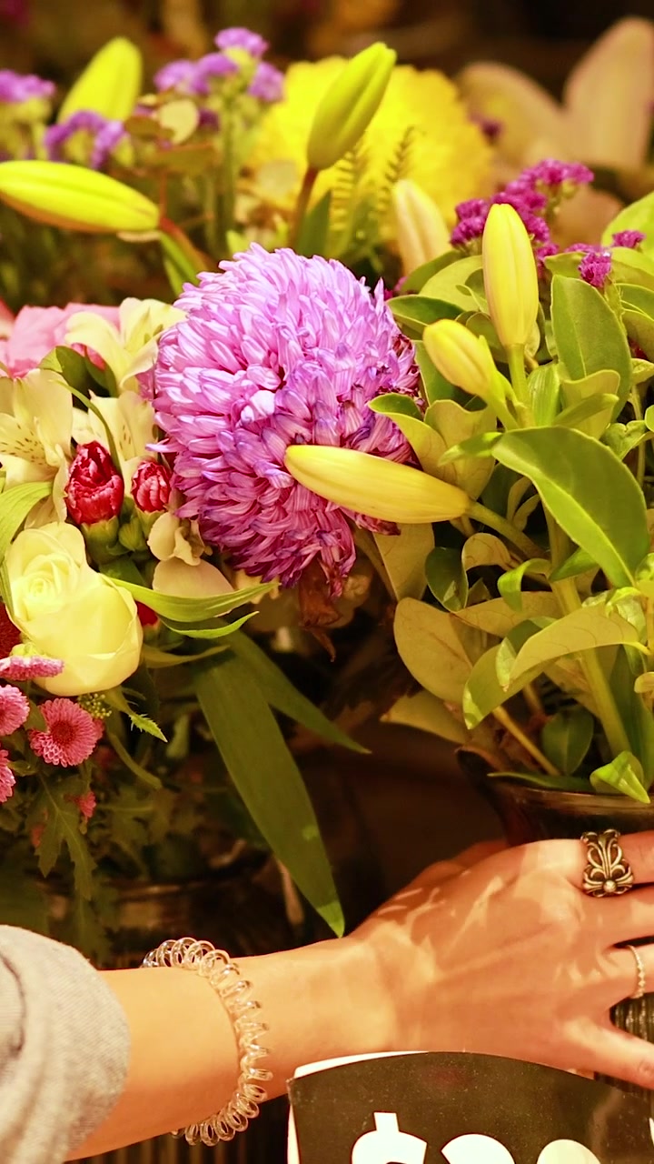 Una persona esamina e seleziona fiori colorati in un ambiente di mercato illuminato calorosamente.