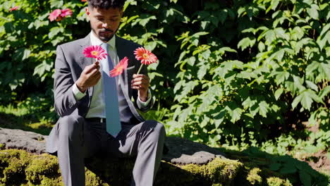elegant man in suit sitting outdoors with pink and orange flowers