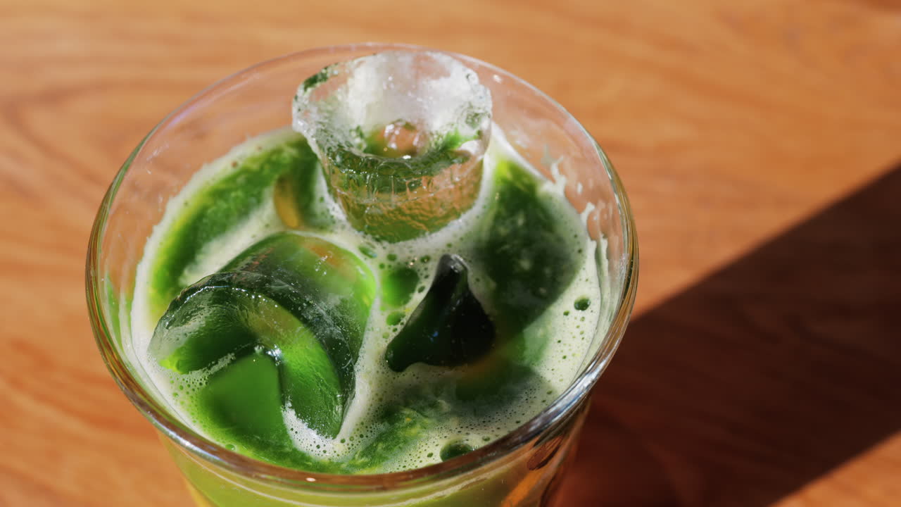 Close up of a glass of an iced orange juice matcha on a table at a cafe