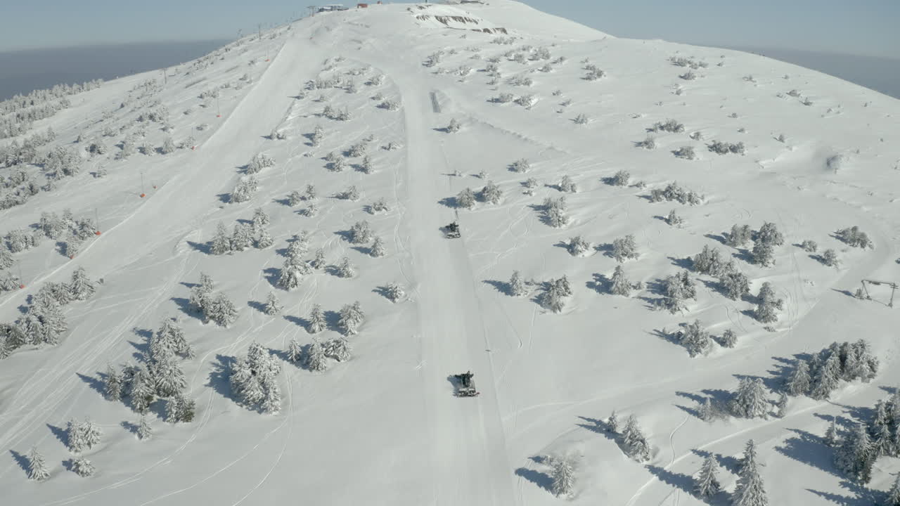 Aerial view of snowcats grooming a ski slope on a snowy mountain