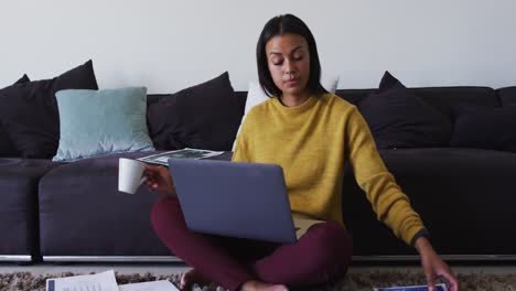 Mixed-race-woman-sitting-on-floor-using-laptop-going-through-paperwork