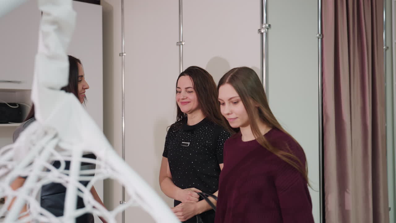 두 명의 백인 여성이 핸드백을 들고 미소를 지으며 부티크 살롱으로 걸어 들어가 채팅하고 있어요. 현대적인 장식과 흔들의자가 보이며, 도시적인 라이프스타일 분위기, 약속에 대한 낙관, 친근한 탐험이 느껴집니다.