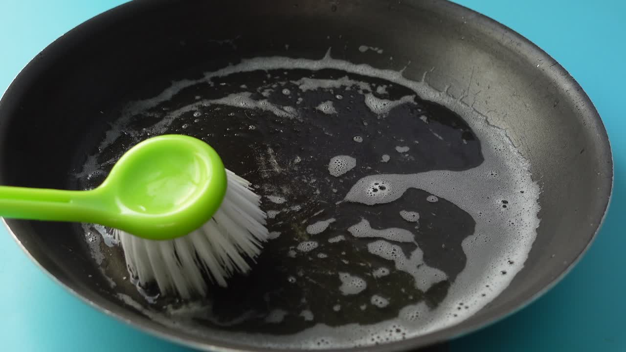 Eine fettige Bratpfanne mit einer Bürste reinigen
