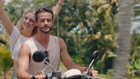 fun couple riding scooter on tropical island happy woman celebrating with arms raised enjoying vacation road trip with boyfriend on motorcycle ride