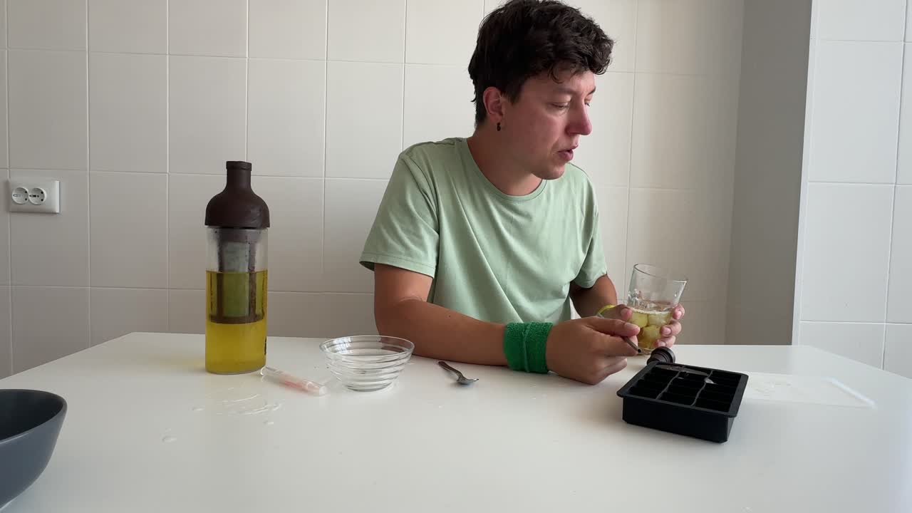 Uomo che beve e mescola una bevanda fredda a un tavolo da cucina.